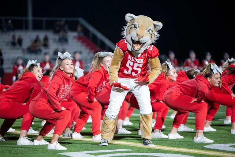 cheerleaders in red uniforms performing on the football field with their tiger mascot dancing with them