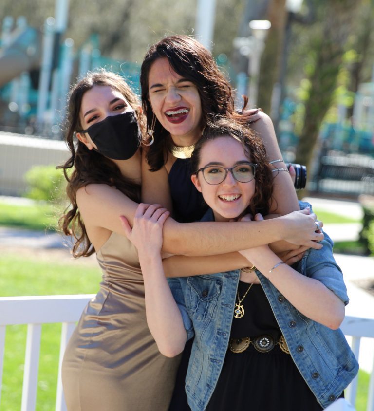 Three students outside hugging each other and smiling