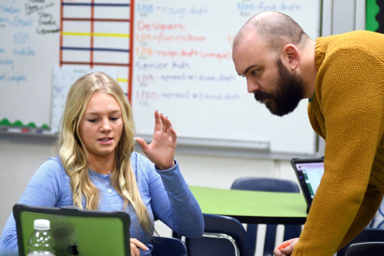 Tucker leans over a desk to help a student.