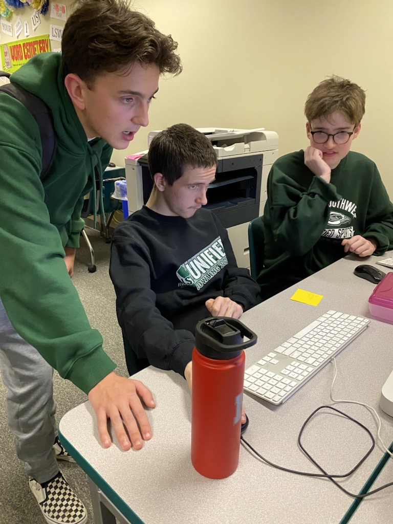 three yearbook students looking at a computer screen working on the yearbook